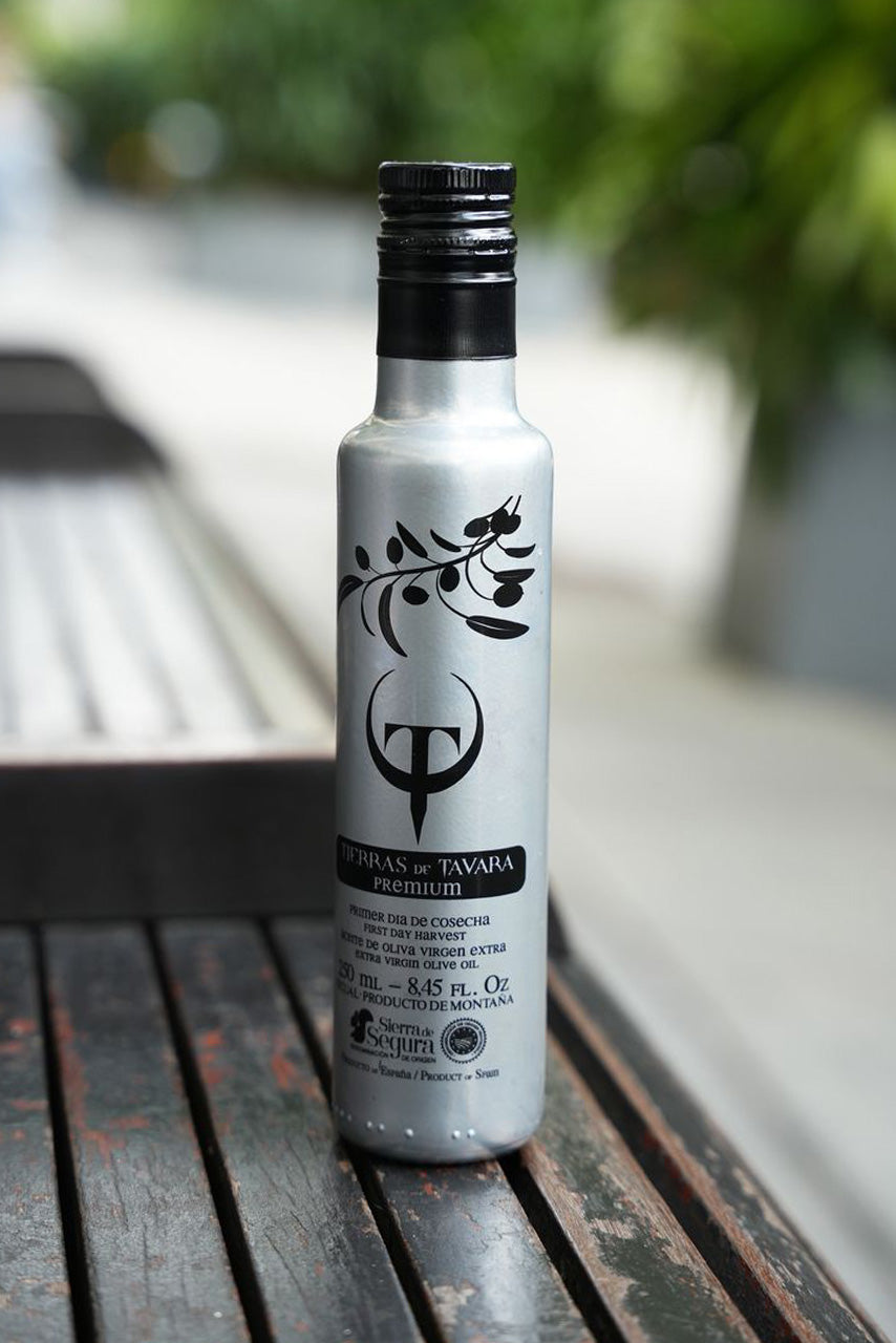 Silver Olive Oil bottle with black cap on a wooden surface outdoors