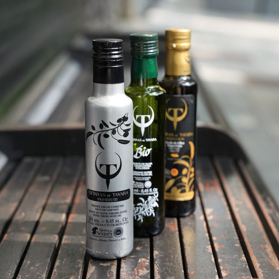 Three bottles of olive oil on a wooden surface with a blurred outdoor background